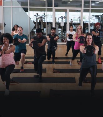 Group of people in a fitness class, each holding a light weight plate and lunging with their left foot forward