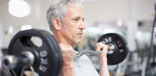Man in grey shirt holds barbell to chest with arms bent