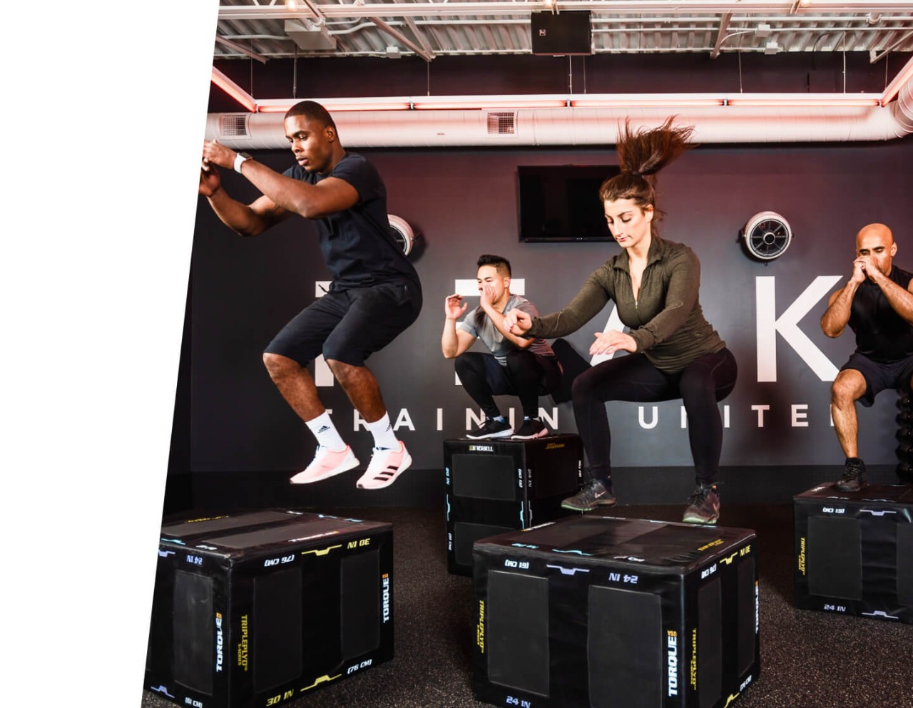 Four people doing box jumps onto black boxes in PEAK training space