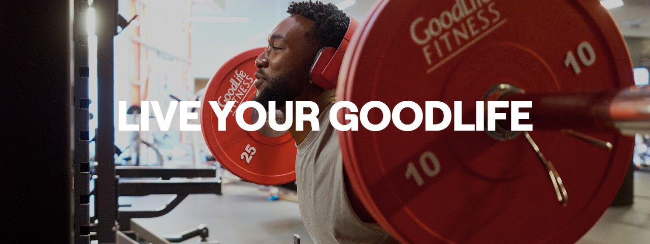 A GoodLife Fitness member wearing red headphones is doing a squat lift with large red weights on a barbell.